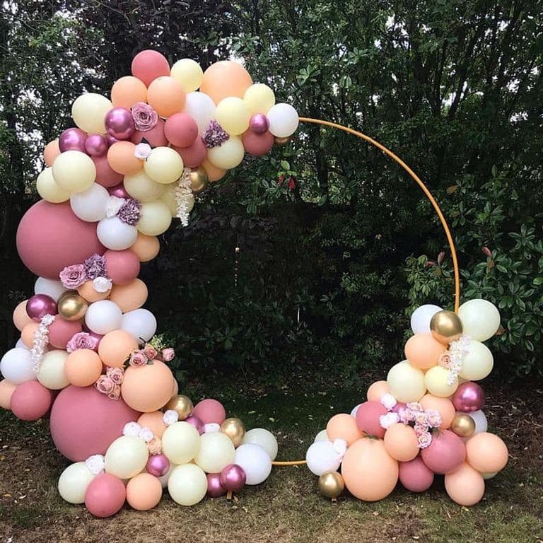 Outdoor circular hoop arch in dusty rose, cream, peach and chrome gold with flowers, set on grass against garden trees