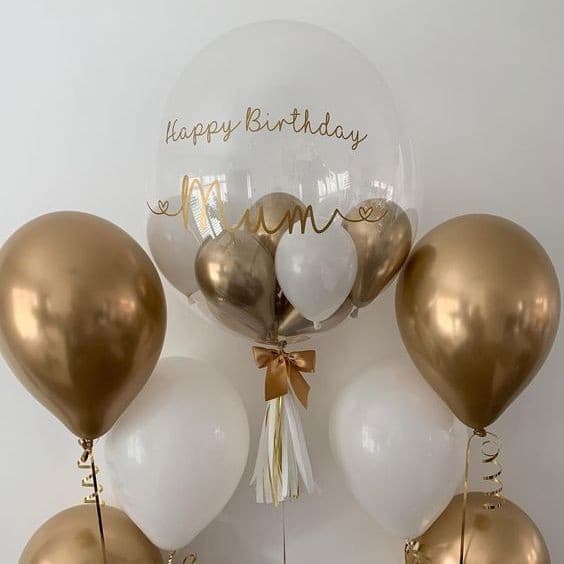 Personalized clear bubble balloon reading Happy Birthday Mum in gold script, in a bouquet of chrome gold and white balloons