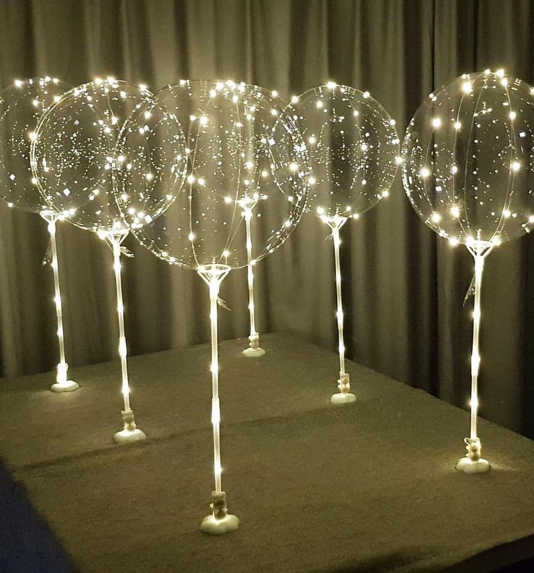 Clear bubble balloons wrapped in fairy lights on tall stands, glowing in a darkened event room